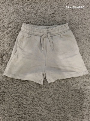 Gröna shorts med snörning - Säljer ett par gråa gröna shorts med elastisk midja och snörning framtill. Shortsen har en avslappnad passform och är tillverkade i mjuk bomull, perfekta för varma dagar. Två sidofickor ger en casual vibe.