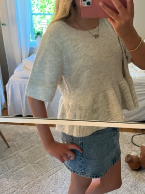 Beige  volangstickad topp - Supersöt beige  stickad topp med volangkant nedtill och korta ärmar. Toppen har en avslappnad passform och rund halsringning. Perfekt att styla med jeanskjol eller shorts för en chill look. (Kan prata om pris)