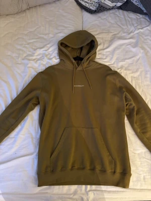 Olivgrön hoodie med tryck - Snygg olivgrön hoodie med huva och dragsnören. Framtill finns en känguruficka och ett diskret vitt tryck på bröstet. Endast använd två gånger. Storlek M.
