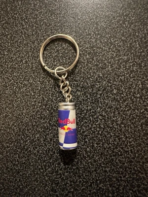 Nyckelring med Red Bull-detalj - Säljer en unik nyckelring med en miniatyr av en Red Bull-burk som hänge. Färgerna är blå, silver, röd och gul. Perfekt accessoar för dig som gillar energidrycker och vill ha något personligt på nyckelknippan. Tillverkad i metall och plast.