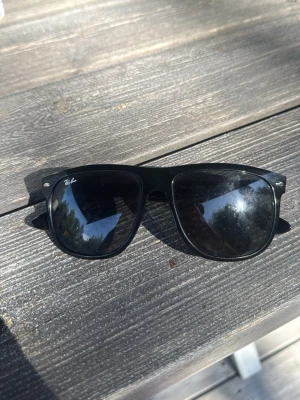 Svarta Ray-Ban Wayfarer solglasögon - Klassiska svarta Ray-Ban Wayfarer solglasögon med bred båge och mörka glas. Snygg och tidlös design som passar till allt. Ray-Ban-loggan syns tydligt på båda skalmarna och i ena hörnet av glaset. Perfekta för soliga dagar.