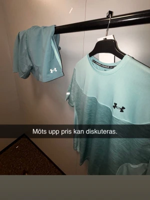 Ljusblått träningsset från Under Armour - Säljer ett ljusblått träningsset från Under Armour med t-shirt och shorts. Setet är gjort i ett lätt och snabbtorkande material, perfekt för gym eller löpning. T-shirten har rund hals och logga på bröstet, shortsen har logga på benet.
