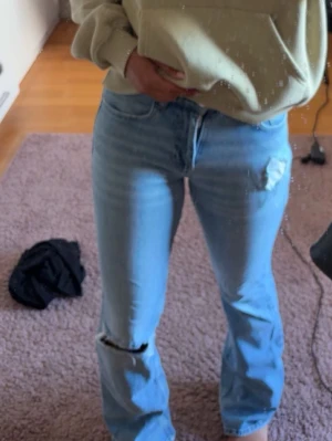 Ljusblå  bootcut jeans från gina tricot - Säljer ett par ljusblå jeans med bootcut-modell och slitningar på knä och lår. Jeansen har klassisk femficksdesign och är tillverkade i denim med lite stretch. Perfekta för en avslappnad och trendig look. Storlek 34. 
