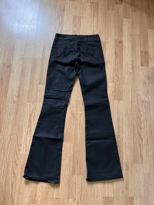 Svarta bootcut jeans med hög midja - Snygga svarta jeans med bootcut passform och hög midja. Jeansen har klassiska fem fickor, dubbla knappar framtill och markerade sömmar längs benen. Perfekta för en trendig och avslappnad stil.