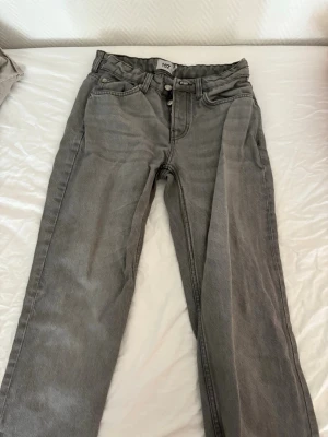 Grå raka jeans med hög midja - Snygga grå jeans med raka ben och hög midja. Klassisk femficksmodell med knapp- och dragkedjegylf. Jeansen har en avslappnad passform och är perfekta för en trendig vardagslook. Går och diskutera pris