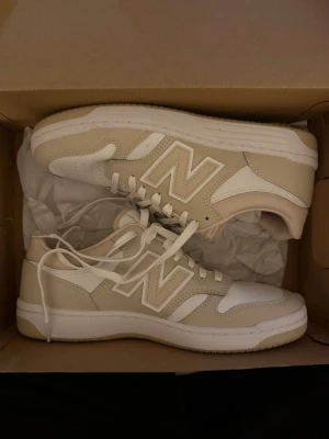 Beige och vita New Balance sneakers - Använd endast en gång. Sneakers från New Balance i beige och vitt. Skorna har klassisk låg modell med vita snören. Syns inte att det har använts då jag hade de en gång i någon timme.
