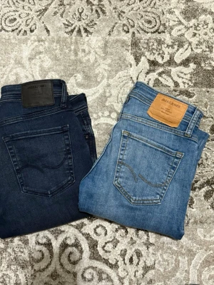 Två par jeans från Jack & Jones - Säljer två par snygga jeans från Jack & Jones, ett par i mörkblå denim och ett par i ljusblå tvätt. Båda har klassisk femficksdesign och skinnpatch bak i midjan. Perfekta för dig som gillar stilrena och tidlösa jeans. Den mörkblåa är i storlek W30 L32 och den ljusblå är i storlek W28 L32