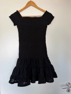 Kort volangklänning - Svart off shoulder klänning med smock och volang. Aldrig använd, endast provad. 