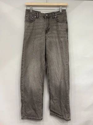 Grå raka jeans  - Säljer ett par grå jeans med rak passform och hög midja. Jeansen har klassisk femficksdesign, bälteshällor och knappgylf. Materialet är denim i 100% bomull och färgen är tvättad grå. Perfekta för en avslappnad och trendig look.
