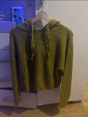 Olivgrön stickad hoodie med snörning - Säljer en olivgrön stickad hoodie med långa ärmar och huva. Tröjan har snörning i halsen och är ribbstickad för en chill och avslappnad look. Perfekt för dig som vill ha något mysigt och snyggt till vardags. Är i storlek L men känns mer som M/S