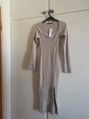 Beige ribbad långklänning Gina Tricot - Säljer en beige ribbad långklänning från Gina Tricot. Klänningen har lång ärm, v-ringad hals och en snygg slits framtill. Perfekt för dig som gillar en slim passform och stilren look.