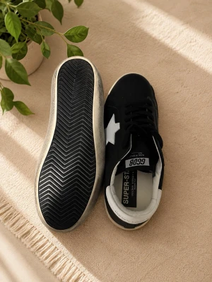 Golden goose sneakers - Stilrena svarta sneakers från Golden goose med vit stjärndetalj på sidan och vit häl. Skorna har svarta skosnören, vit sula och är tillverkade i slätt material. Perfekta för dig som gillar en klassisk men trendig look.