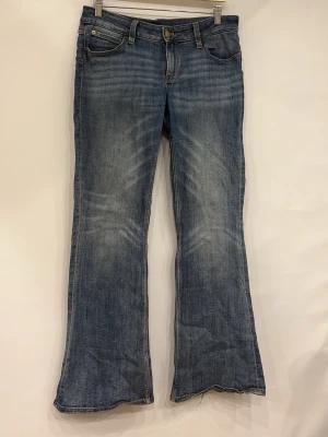Blå bootcut jeans med slitningar - Säljer ett par blå bootcut jeans med snygga slitningar och tvättade detaljer. Jeansen har klassisk femficksmodell, normal midja och rå kant längst ner på benen för en trendig look. Perfekta för dig som gillar en avslappnad men ändå stilsäker stil.