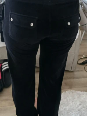 Svarta mjukisbyxor Juicy Couture - Säljer ett par svarta mjukisbyxor i mjuk velour med raka ben och dragsko i midjan. Byxorna har två fickor bak med silverfärgade knappar och en ganska vid passform. Perfekta för när du vill vara extra bekväm.❤️😊 Jag bär S och byxorna passar väldigt bra även fast storleken är XS!