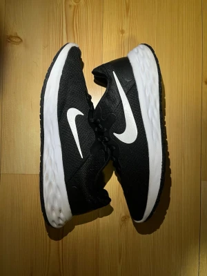 Svarta Nike sneakers med vit sula - Snygga svarta Nike sneakers med vit sula och vit swoosh-logga på sidan. Ovandelen är i meshmaterial som andas och sulan är lätt och dämpande. Perfekta för en sportig och stilren look. Skriv vid frågor, flexibel med priset!