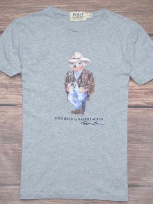 Grå Polo Bear t-shirt från Ralph Lauren denim supply - Snygg grå t-shirt från Ralph Lauren med det ikoniska Polo Bear-motivet på bröstet. Björnen har cowboyhatt, brun jacka och jeans. T-shirten har rund hals och korta ärmar, perfekt för en avslappnad stil.