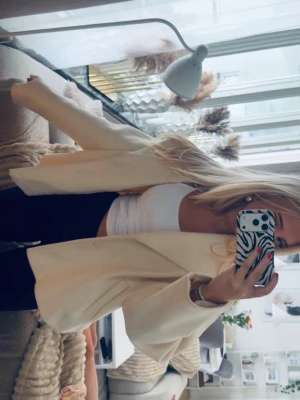 Oversized beige kavaj - Stilren oversized beige kavaj med breda slag och rak passform. Kavajen har en minimalistisk look utan synliga knappar och är tillverkad i ett slätt tyg som ger en modern känsla. Perfekt att styla med crop top och jeans för en trendig outfit.