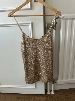 Glittrigt guldigt linne med paljetter - Säljer ett glittrigt linne från Esprit i guld med tunna axelband och täckt av paljetter. Perfekt för dig som vill sticka ut och glänsa. Linnet har en rak passform och är fodrat på insidan för extra komfort. köpt för 699kr!