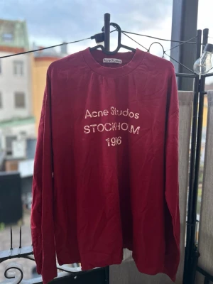 Vinröd sweatshirt Acne Studios - Vinröd långärmad sweatshirt från Acne Studios med tryck 'Acne Studios STOCKHOLM 1996' i vitt på bröstet. Klassisk rund halsringning och avslappnad passform. Perfekt för en trendig och avslappnad stil.