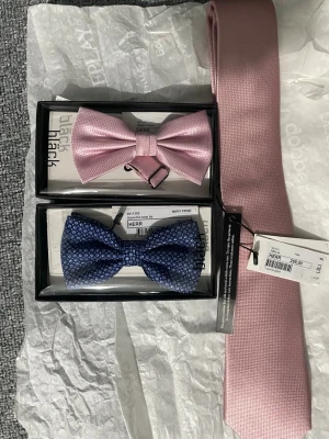 Rosa slips och två flugor - Säljer en stilren rosa slips samt två flugor, en i ljusrosa och en i blått med diskret mönster. Perfekta accessoarer för att lyfta din outfit och ge en elegant touch. Passar till skjorta och kavaj för en dressad look.