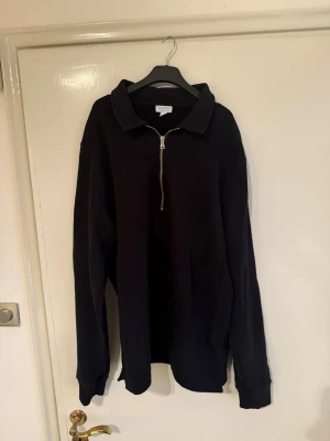 Svart halvzip tröja med krage - Säljer en svart hoodie med halv dragkedja och klassisk krage. Hoodien har långa ärmar och ribbade muddar vid ärmslut och nederkant. Perfekt för en avslappnad och stilren look. Materialet känns mjukt och bekvämt.