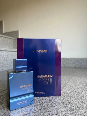 Haramain Amber Oud Dubai Night parfym - Exklusiv parfym från Al Haramain, Amber Oud Dubai Night. Flaskan är elegant i metallicblått med guldtext och har en fyrkantig form. Kommer i en lyxig lila och blå förpackning. Perfekt för dig som gillar unika och intensiva dofter.
