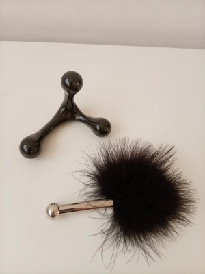 Massageverktyg och fluffig fjäderstick - Säljer ett set med ett svart massageverktyg i plast med tre rundade ändar och en fluffig svart fjäderstick med metallhandtag. Perfekt för avslappning och skön massage. Båda är lätta att använda och har en modern look.