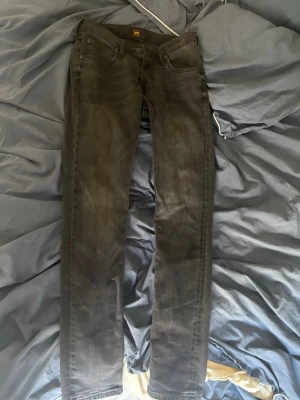 Svarta skinny jeans från Lee - Säljer ett par svarta skinny jeans från Lee med klassisk femficksdesign och låg midja. Jeansen har en smal passform och är tillverkade i stretchigt denimtyg för extra komfort. Perfekta för dig som gillar en stilren och enkel look.