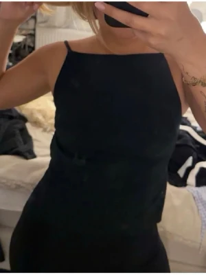 Svart ärmlös linnetopp med öppen rygg - Snygg svart linnetopp med smala axelband och öppen rygg. Toppen har en minimalistisk design och sitter tight mot kroppen, perfekt för en trendig look. Passar till både jeans och kjol för en stilren outfit. Första bilden är lånad, lapp är borta men den jag köpte av stod det Gina tricot