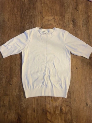 Vit kortärmad topp i bomull - En stilren vit topp med korta ärmar och rund hals. Toppen har ribbade detaljer vid ärmslut och nederkant, vilket ger en snygg finish. Perfekt att matcha med jeans eller kjol för en enkel och fräsch look.