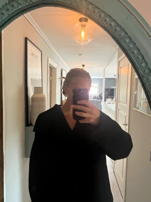 Svart kappa - Snygg svart kort kappa, markerad krage och rak passform. Rocken har en minimalistisk design utan synliga knappar framtill och är fodrad på insidan. Perfekt för dig som gillar stilrena och tidlösa plagg.