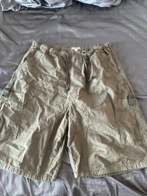 Khaki cargo shorts från Jaded London - Säljer ett par khaki cargo shorts från Jaded London i oversized modell. Shortsen har flera fickor, snörning i midjan och är tillverkade i bomull. Perfekta för en avslappnad och trendig stil. Helt oanvända och prislapp kvar. Nypris: 759kr