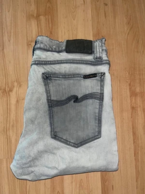 Nudie jeans  - Säljer ett par ljusgrå skinny jeans från Nudie Jeans med svarta kontrastsömmar. Midja 39cm, längd 109cm. OBS jeansen har 2 defekter: tyget är lite förtunnat samt slitna längst ned vid benöppningen.  Ifall det inte finns någon bild i annonsen där jag bär plaggen jag säljer så är det för att jag ej kan ha storleken heller passformen, så kolla måtten för storlek och googla på modellnamnet för passform 😉 s6,1