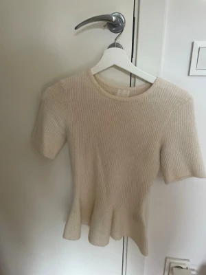 Ribbad beige topp med kort ärm - Säljer en ribbad beige topp med korta ärmar och rund hals. Toppen har en lätt utsvängd nederkant och är gjord i ett mjukt stickat material. Perfekt för dig som gillar en enkel men ändå stilren look.