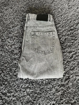 Grå mom jeans från Levi's - Säljer ett par grå mom jeans från Levi's med hög midja och raka ben. Klassisk femficksmodell i tvättad denim som ger en avslappnad vintagekänsla. Perfekta för dig som gillar en retro och trendig stil.