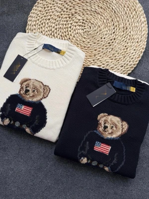 Stickad tröja med björn och USA-flagga - Säljer en stickad tröja med en söt björn på bröstet som har en tröja med amerikanska flaggan. Finns i både mörkblått och vitt. Tröjan har rund hals, ribbade muddar och är perfekt för dig som gillar coola detaljer och klassisk stil.