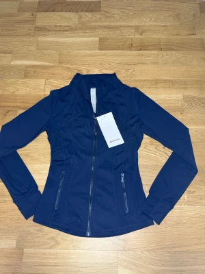 Mörkblå Nulu define jacket Lululemon i Stl.4 - Den lite mindre och smalare versionen av lululemons define jacket I Stl 4 som motsvarar runt S eller en riktigt tight M. Jag hade rekommenderat S för bäst passform. Den är helt oanvänd och ren!💞💞