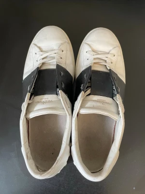 Valentino opens - Snygga vita sneakers från Valentino med svart läderdetalj över mitten. Klassisk låg modell med rund tå och vita snören. Skorna har en stilren och modern design, perfekt för dig som gillar snygga och exklusiva märken🙌| Bra skick med enstaka defekter (syns på bild 4) och innersulan är bytt för bättre kvalitet.⭐️