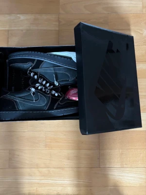 Sneakers: Travis Scott x Air Jordan 1 Low OG 'Black Phantom - Det här är de mycket eftertraktade Travis Scott x Air Jordan 1 Low OG 'Black Phantom'-sneakersen, med en elegant ovandel i svart mocka och läder med distinkta vita kontrastsömmar.  De levereras komplett med originalförpackningen, extra röda snören och den matchande svarta paisleybandanan, som visar upp den ikoniska omvända Swoosh-loggan och Cactus Jack-loggan. Storlek:44  Skick: 10/10  Färg: Svart  Snabb och noggrann leverans.