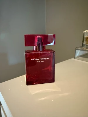 Narciso Rodriguez For Her parfym intense 30 ml - En elegant parfymflaska i mörkrött glas från Narciso Rodriguez, modellen 'For Her intense'. Flaskan har en stilren, fyrkantig form med matchande röd kork och vit text på framsidan. Perfekt för dig som gillar exklusiva och moderna dofter. Förvarats mörkt och svalt