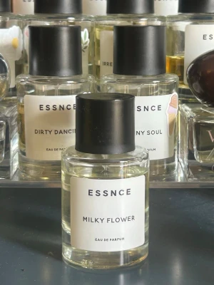 ESSNCE Milky Flower Eau de Parfum - Minimalistisk parfymflaska från ESSNCE med doften Milky Flower. Flaskan är cylindrisk i genomskinligt glas med svart plastlock och vit etikett med enkel text. Innehållet är ljusgult och ger ett stilrent intryck.