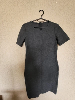 Mörkgrå kort klänning med kort ärm - Stilren mörkgrå klänning i enkel design med rund halsringning och korta ärmar. Klänningen har en rak passform och är tillverkad i ett mjukt material som ger en bekväm känsla. Perfekt för dig som gillar minimalistisk stil.