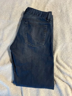 Mörkblå raka jeans - Snygga mörkblå jeans med rak passform och klassiska fem fickor. Jeansen har diskreta slitningar framtill och kontrastsömmar. Perfekta för en avslappnad och stilren look.