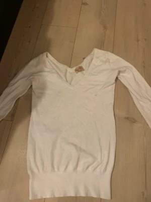 Vit stickad tröja från Bershka - Klassisk vit stickad tröja från Bershka med djup V-ringning och långa ärmar. Tröjan har ribbstickade muddar vid ärmslut och nederkant. Perfekt att matcha med jeans eller kjol för en enkel och stilren look.