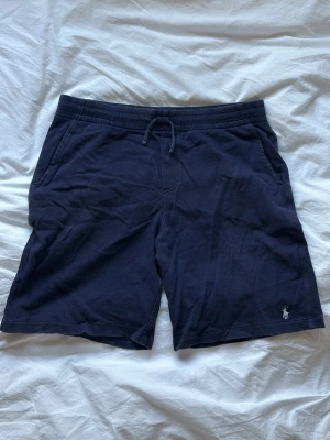 Mörkblå Ralph Lauren shorts  - Snygga mörkblå shorts med snörning i midjan och fickor på sidorna. Tillverkade i mjukt bomullsmaterial och har en Ralph lauren logga på vänster ben. Perfekta för chill dagar eller när du vill ha det bekvämt.