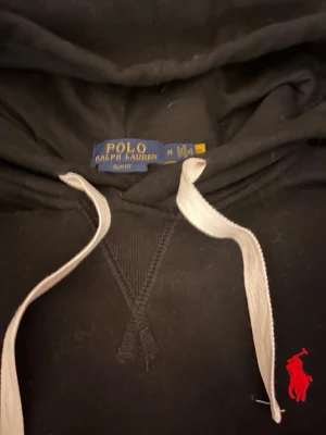 Svart hoodie från Polo Ralph Lauren - Snygg svart hoodie från Polo Ralph Lauren med vit dragsko och den klassiska röda loggan broderad på bröstet. Hoodien har huva och är i en mjuk bomullsblandning, perfekt för en chill och stilren look.Priset går att diskutera vid snabb affär, finn de frågor så är de bara o skriv 😊