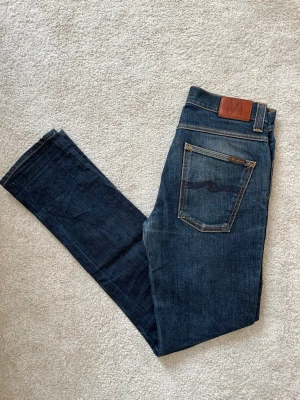 Mörkblå jeans från Nudie Jeans - Ett par riktigt feta jeans ifrån märket Nudie Jeans. Storleken är 32-34 och modellen är Grim Tim. Jeansen har en snygg passform utan defekter! Ifall du vill ha fler bilder så skriv!  😁✌🏼 ——————————————————————————                                                                      📐| Storlek: 32-34                                                  👖| Märke: Nudie jeans                                         🔎| Skick: Fint skick!                                               💵| Ny Pris: 1699kr