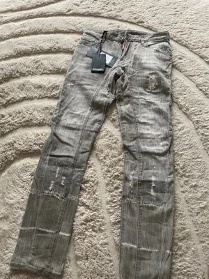 Gråa dsquared 2 jeans  - Säljer ett par grå jeans med slitningar, lagade partier och vita färgstänk för en riktigt edgy look. Jeansen har raka ben och klassisk femficksmodell.  Helt nya 😊