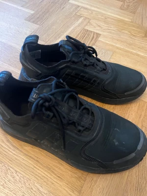 Svarta adidas sneakers med snörning - Snygga helsvarta sneakers med snörning och diskreta detaljer på sidan. Ovandelen är i textil och syntet, med en robust sula och dragflik bak. Perfekta för dig som gillar en clean och sportig look.