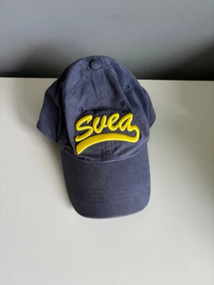 Blå keps med gul Svea-logga - Snygg blå keps från Svea med broderad gul logga framtill. 